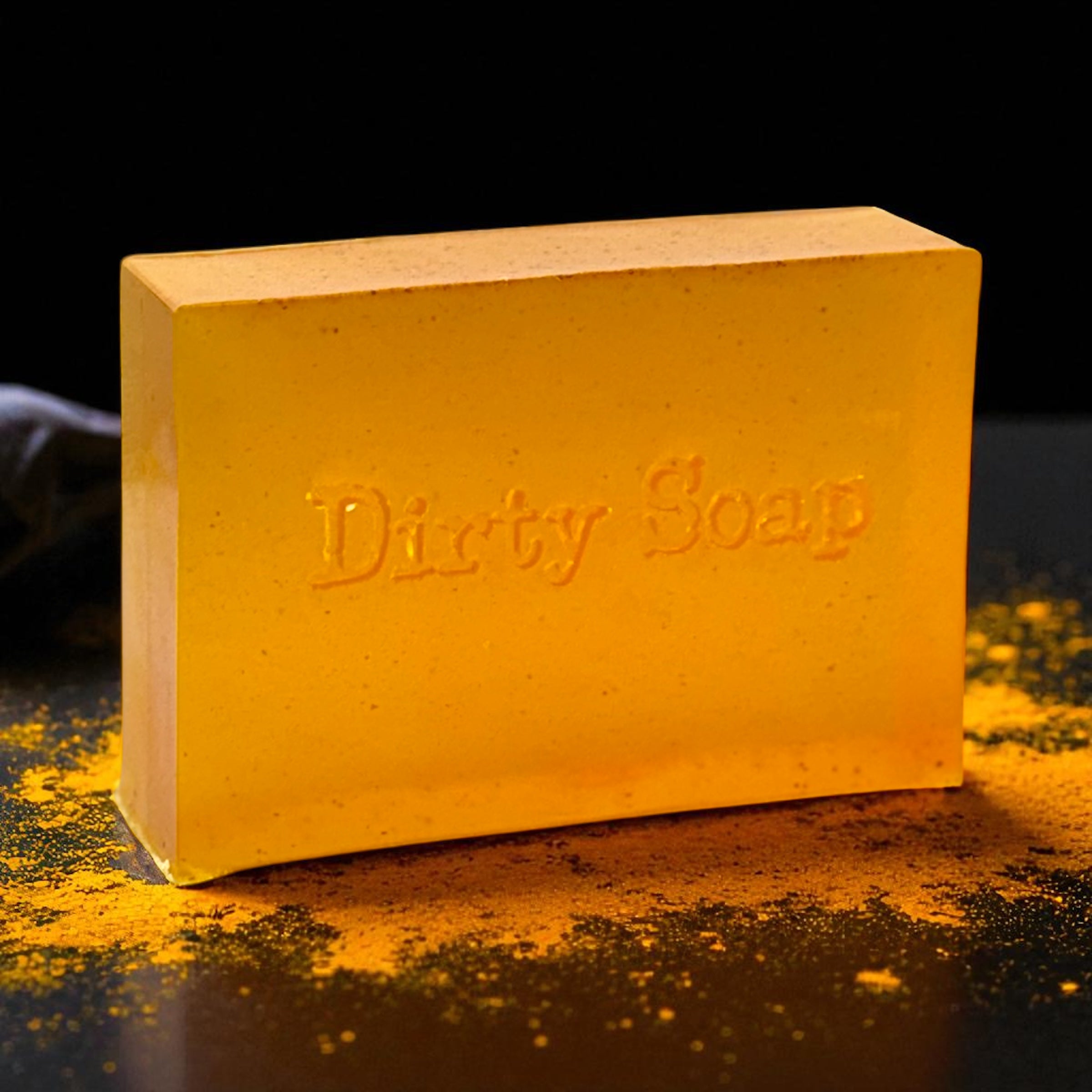 Turmeric soap bar with the text Dirty Soap stamped onto it. Turmeric powder on a black surface
