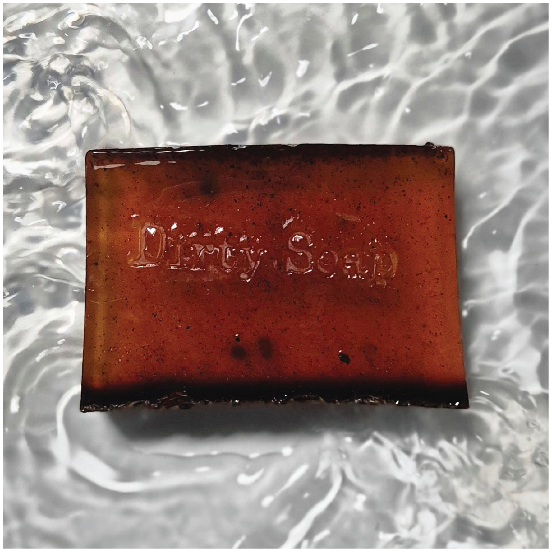 Dark Brown soap bar infused with coffee beans and stamped with a dirty soap logo 
